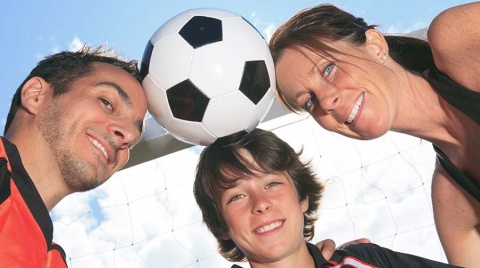 Positive soccer parents and their son holding a soccer ball with their heads